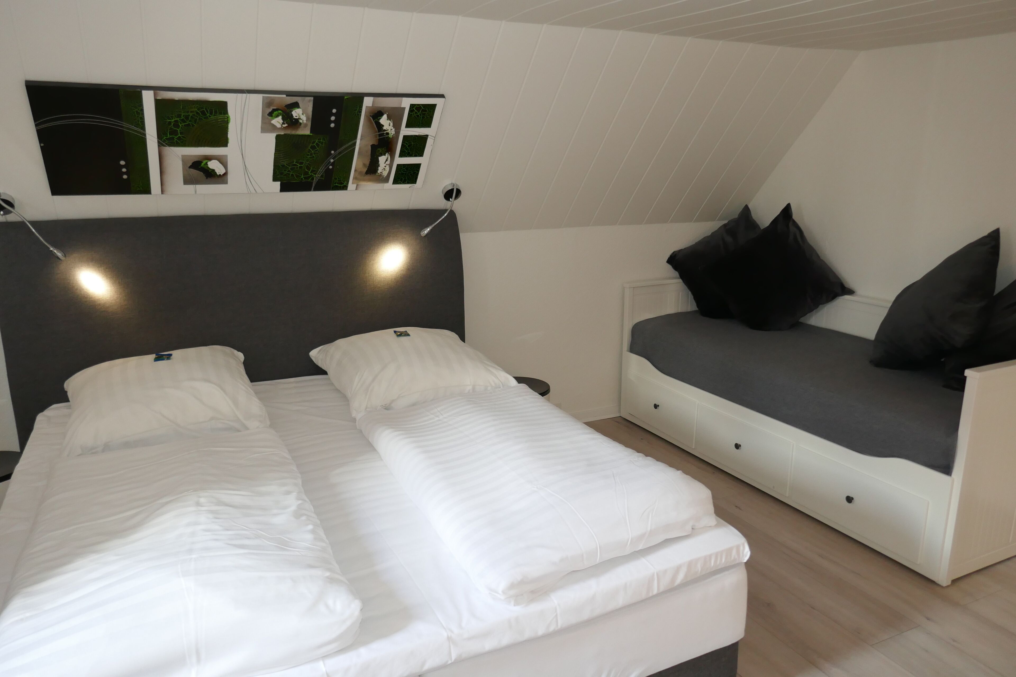 Un dormitorio con dos camas individuales, un sofá y una lámpara fijada a la pared.
