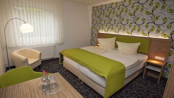 A hotel room with a bed, a chair, a table with bottles, and a patterned wall.