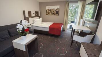 Quarto de hotel com uma cama, uma escrivaninha, um sofá e uma pintura com vista para a cidade na parede.