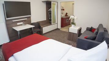 A hotel room with a bed, a desk, a sofa, a TV, a mirror, and a bathroom visible through an open door.
