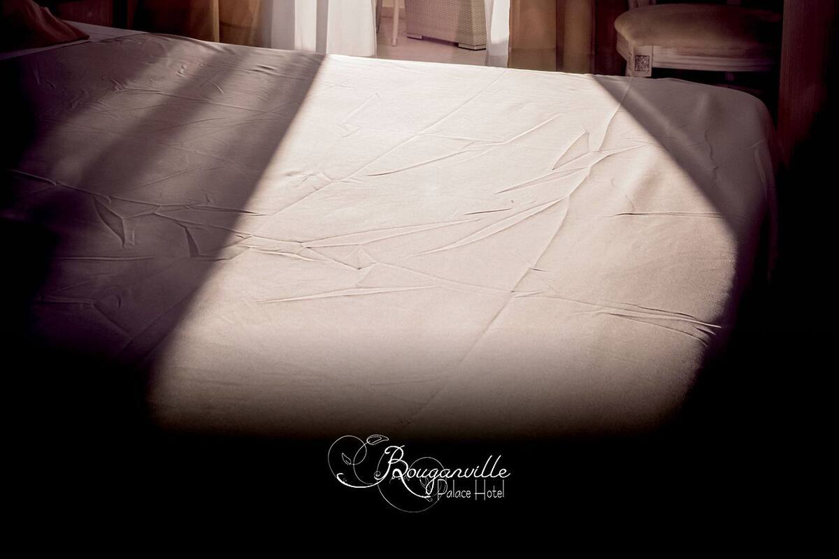 A hotel room with a bed, a chair, and a view of the outdoors through sheer curtains.