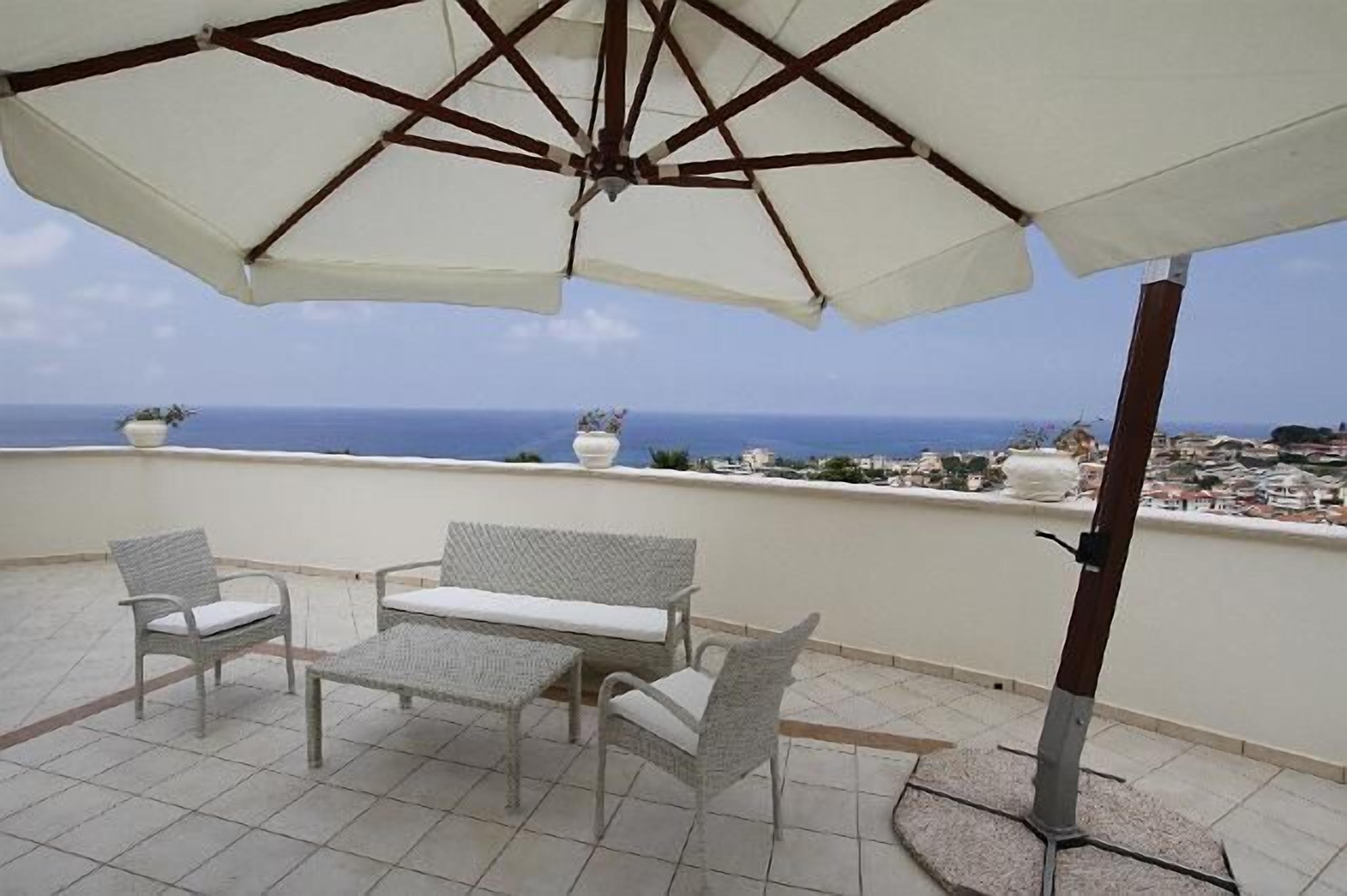 Ein Balkon mit Korbmöbeln, einem großen Sonnenschirm und Meerblick.