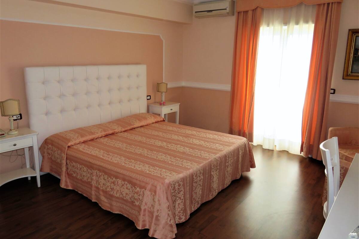 A bedroom with a large bed, a bedside table with a lamp, a nightstand, and a chair.
