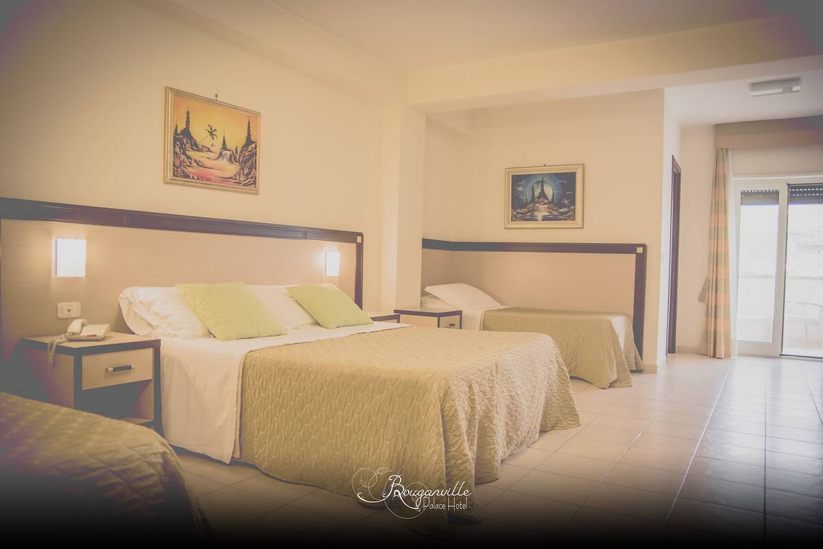 A hotel room with a large bed, a smaller bed, a nightstand with a phone, and two paintings on the walls.