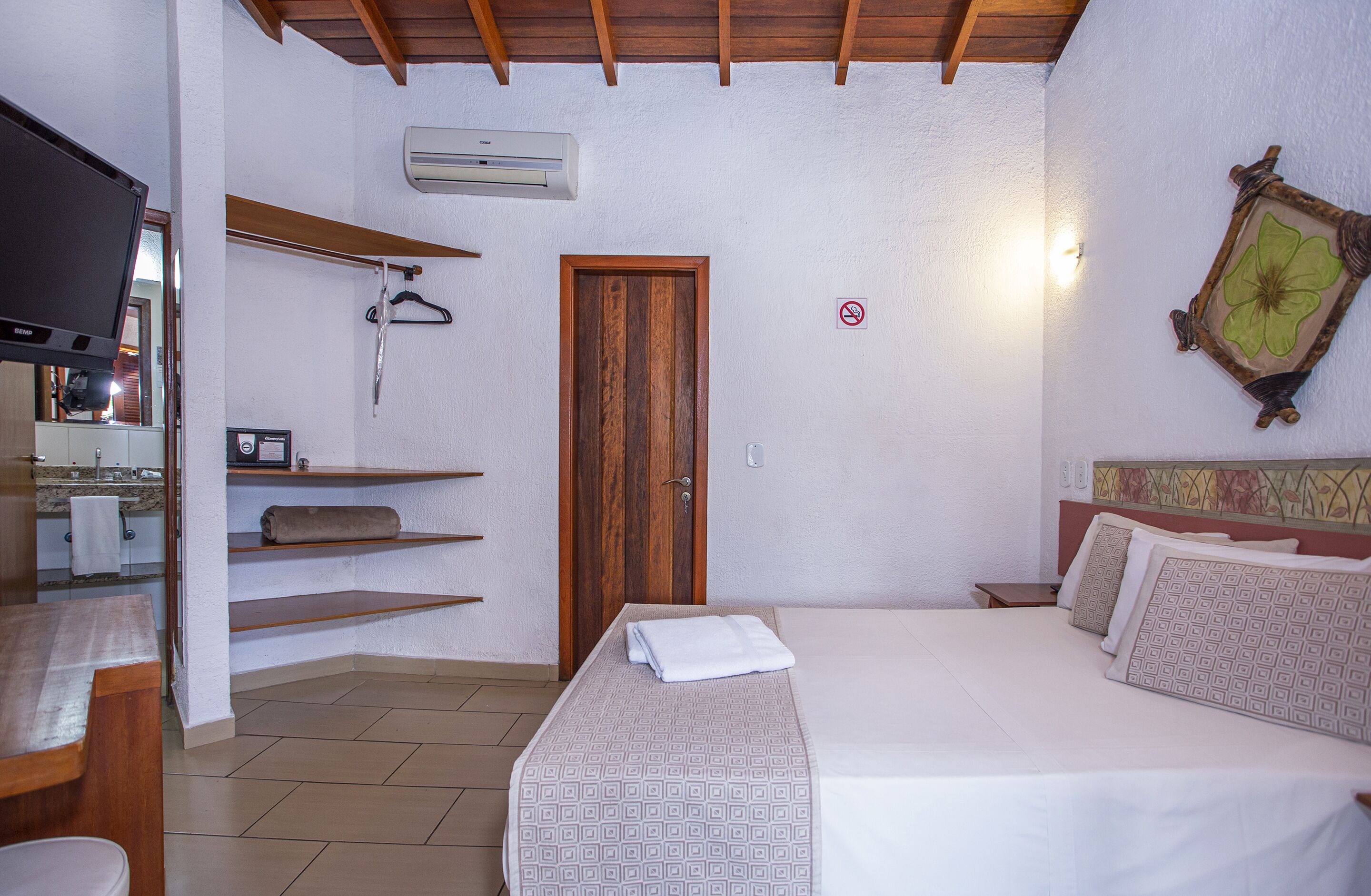 Une chambre à coucher avec un lit, un téléviseur, une porte en bois et un climatiseur fixé au mur.