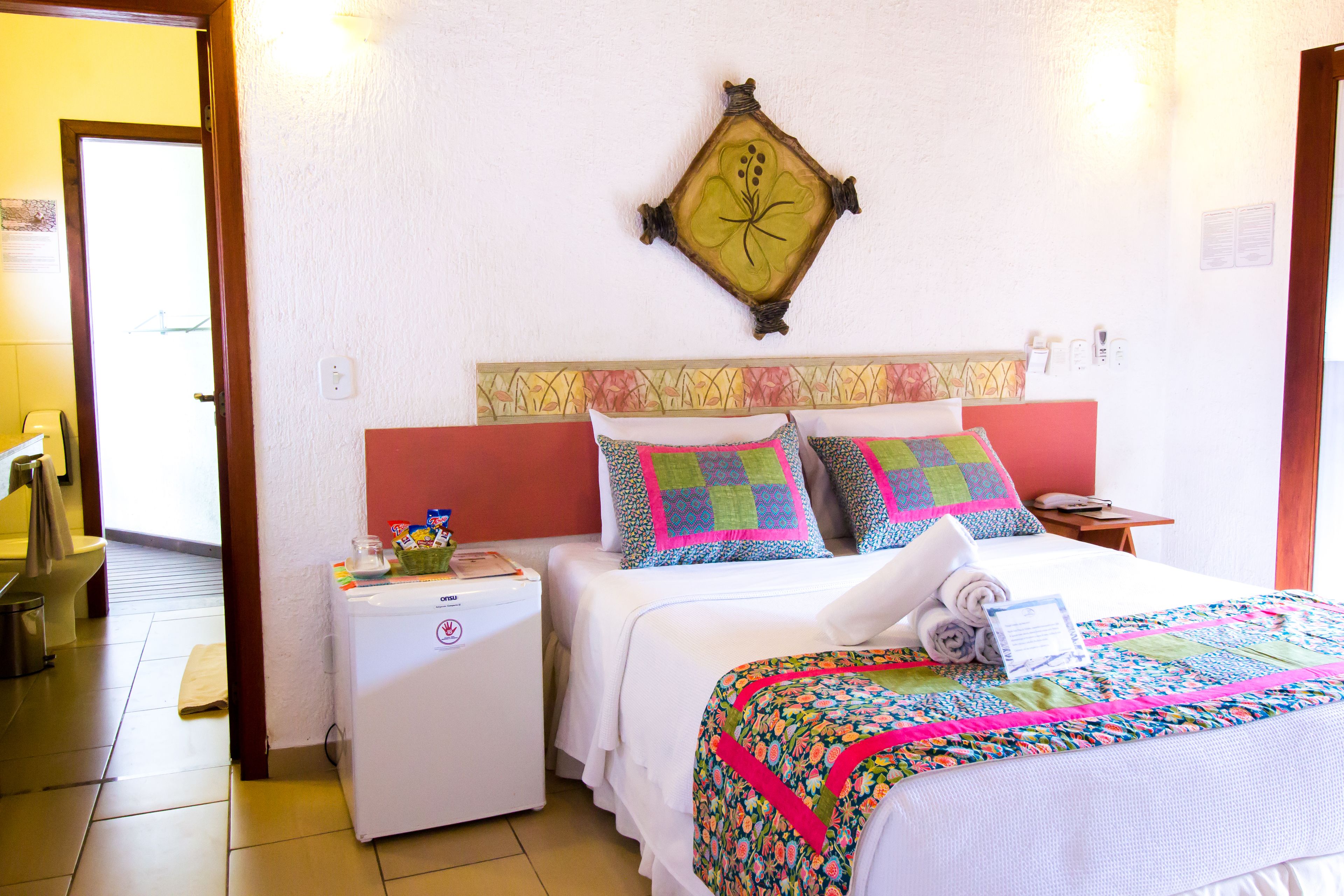 A hotel room with two beds, a small bedside table, a wall-mounted decorative item, and a visible door leading to the bathroom.