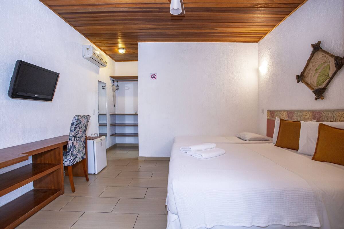 A hotel room with a bed, a desk with a chair, a television, and an air conditioning unit.