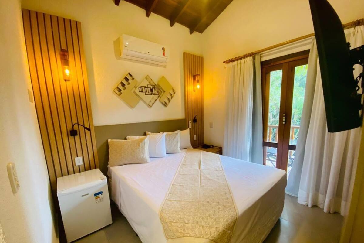 A bedroom with a large bed, a bedside table, a wall-mounted air conditioner, and a window with curtains.