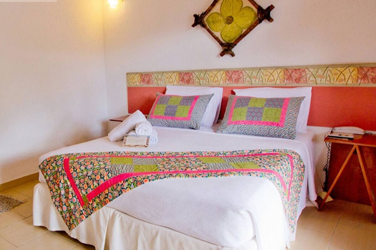 A bed with a floral bedspread, pillows with patterned quilts, and a wall-mounted decorative piece.