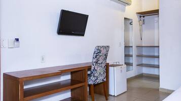 Habitación con escritorio de madera, una silla, televisor, refrigerador pequeño y zona de ducha.