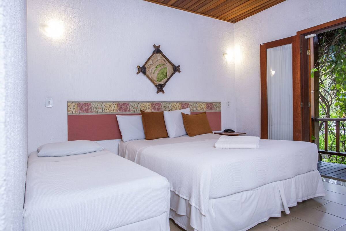 A hotel room with two beds, a decorative wall hanging, and a view of greenery through a sliding door.