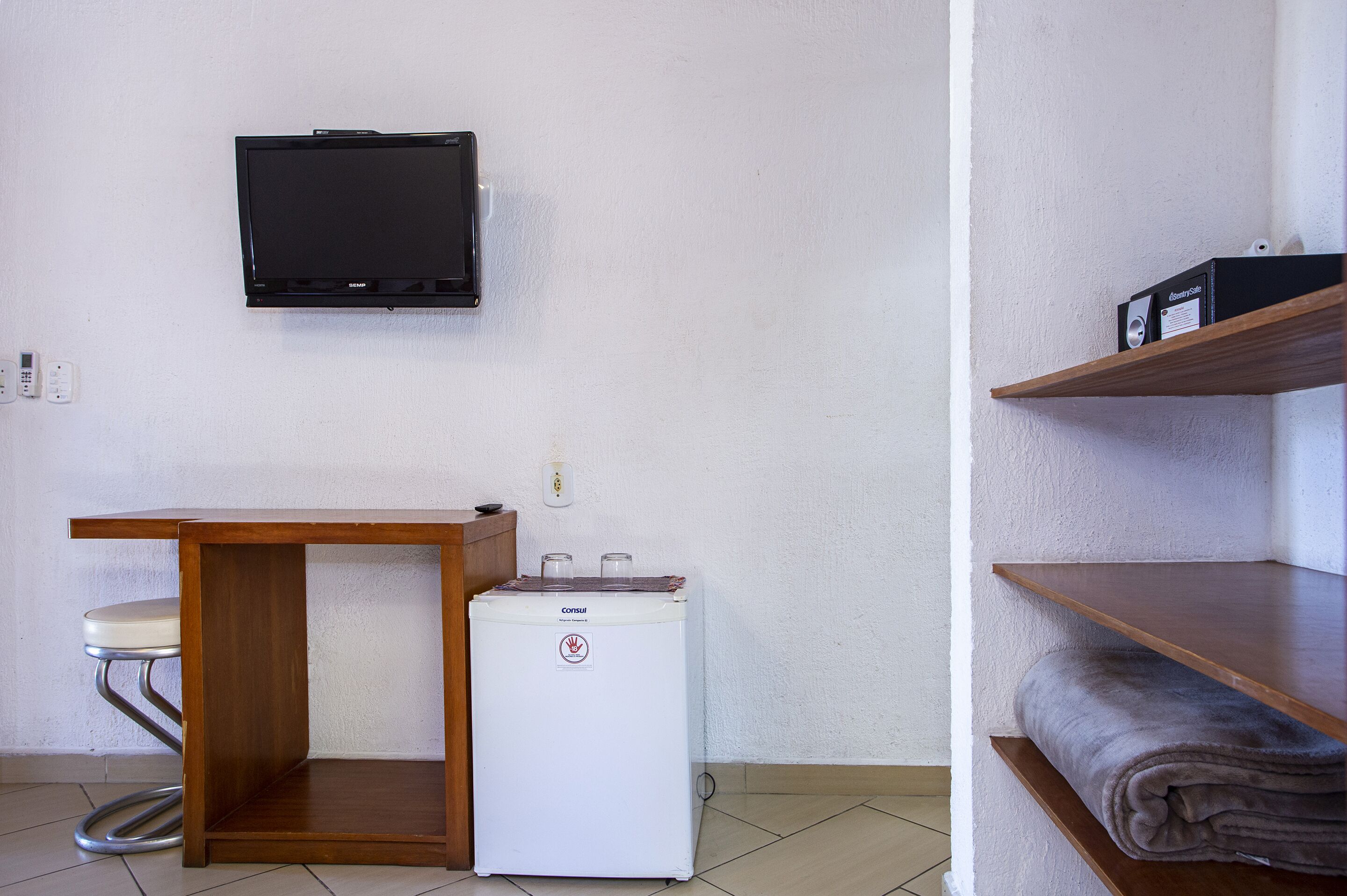 Una habitación pequeña con un escritorio de madera, una lavadora blanca, un televisor instalado en la pared y un estante con una toalla doblada.
