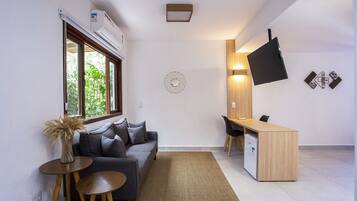 A compact living space with a sofa, a small table, a desk, and a flat-screen TV mounted on the wall.