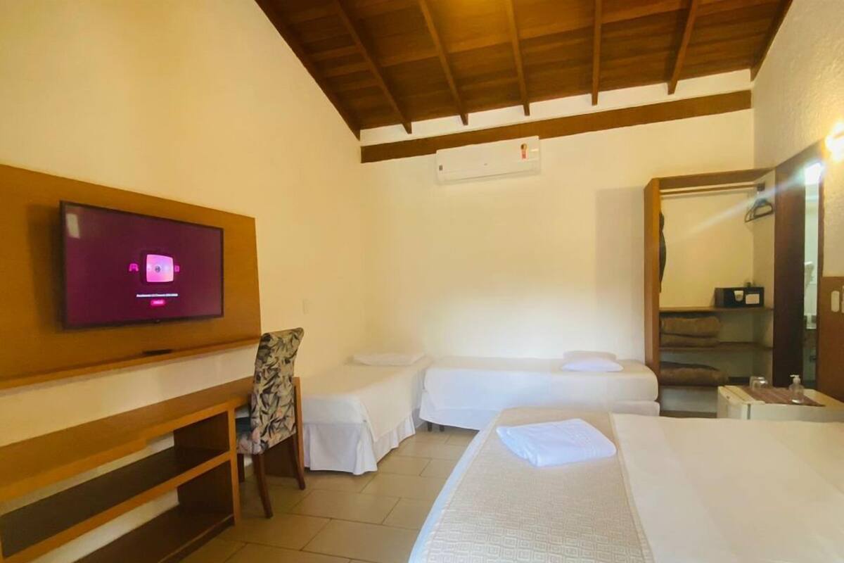 A hotel room with a television, two beds, a chair, and a wardrobe.