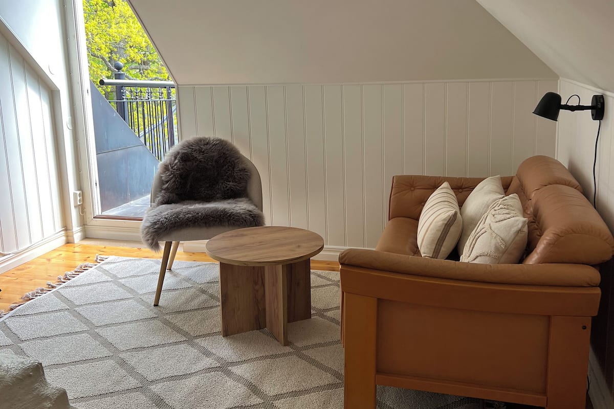 Ein gemütliches Schlafzimmer im Loft-Stil mit Holzboden, einem braunen Sofa, einem flauschigen Sessel und einem kleinen Holztisch.