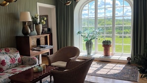 Een gezellige woonkamer met een groot raam, rieten meubels, een houten bijzettafeltje en een groen gestreepte wand.