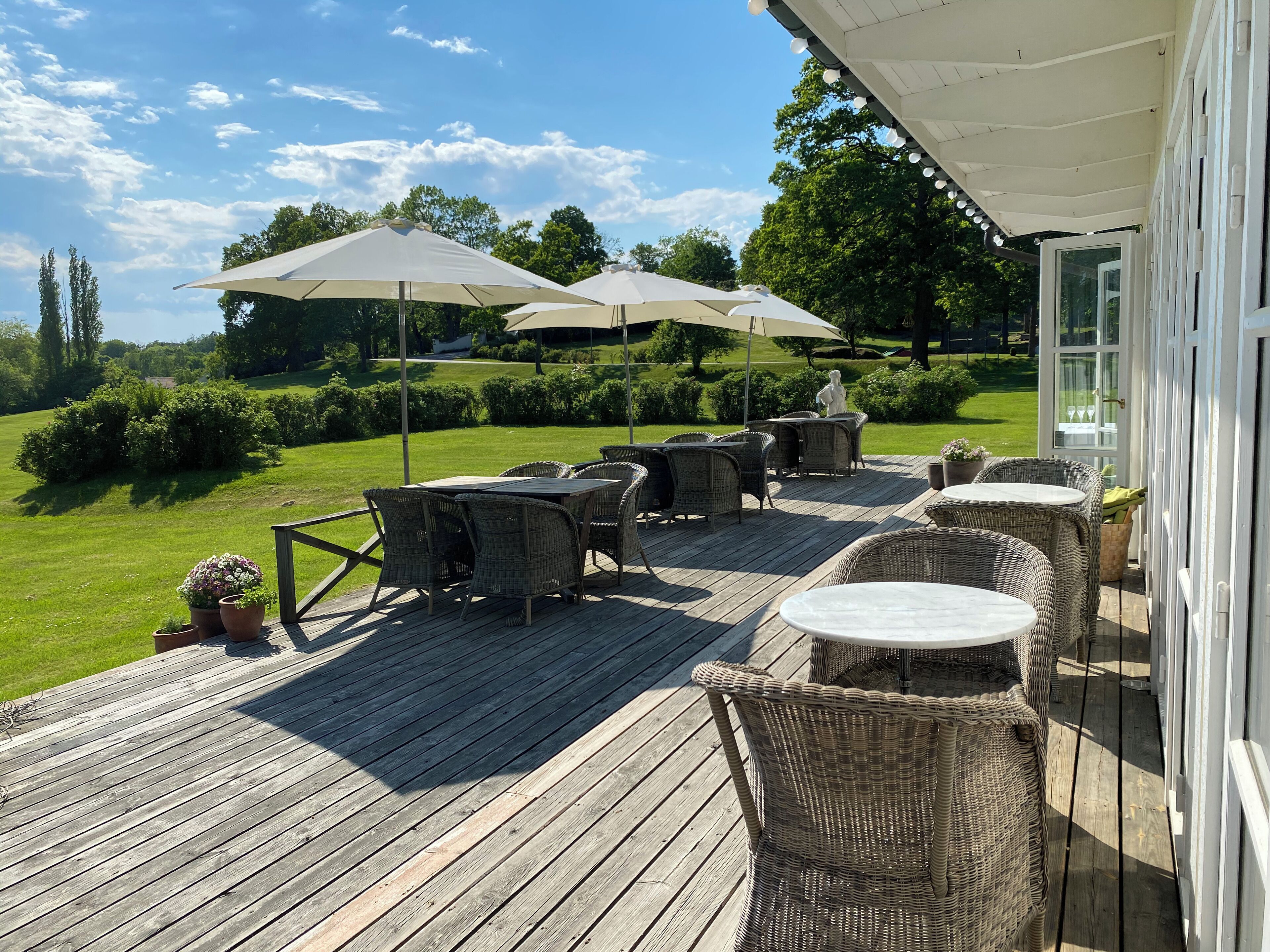 A wooden deck with wicker furniture and umbrellas, overlooking a well-maintained lawn and trees.