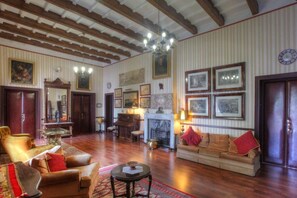 A spacious living room with wooden floors, a fireplace, and a piano. - Hotel del Almirante (Es Castell)