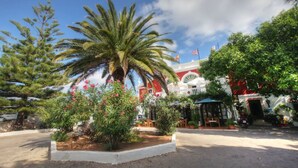 A hotel courtyard with palm trees, a gazebo, and a building with a red and white facade. - Hotel del Almirante (Es Castell)