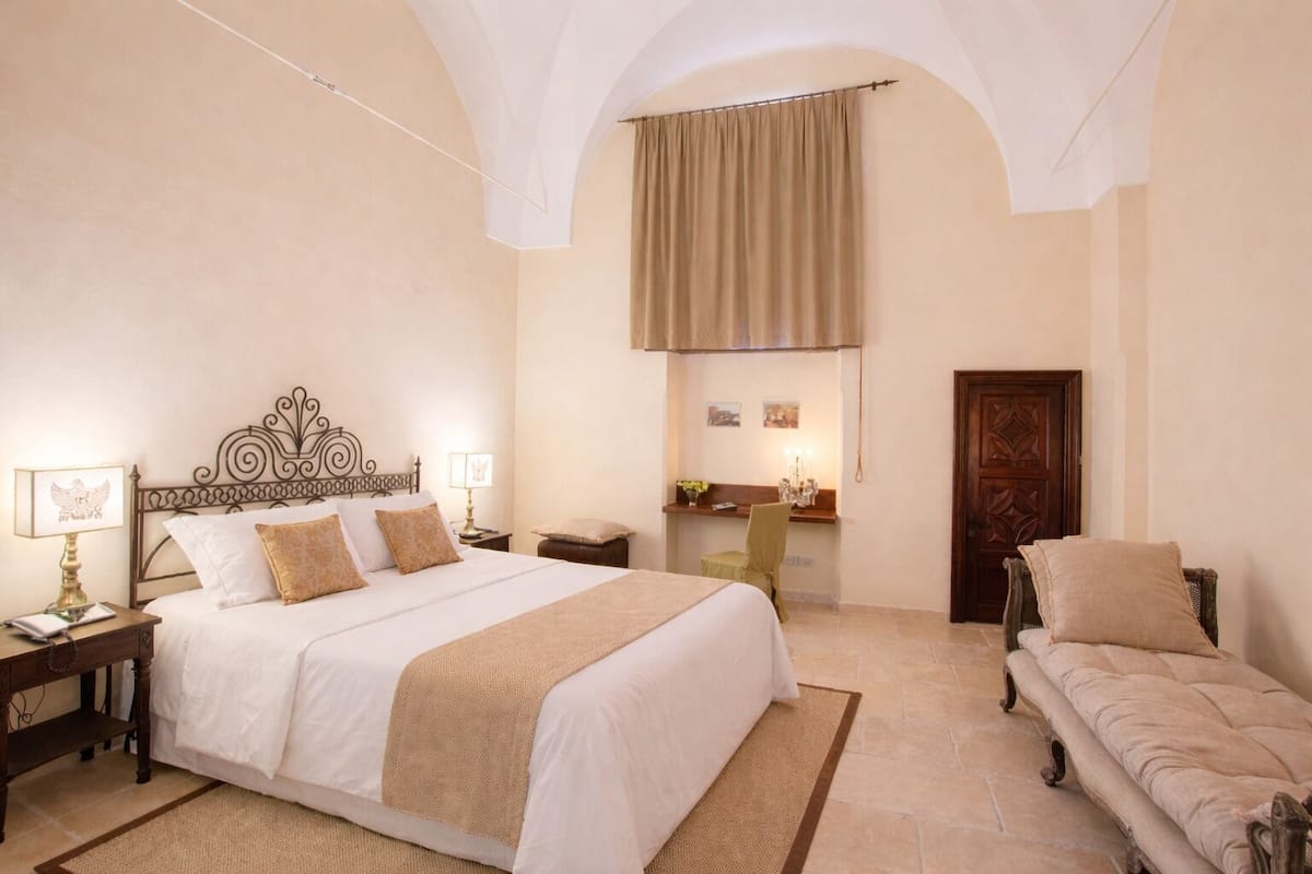 A bedroom with a large bed, a wooden chair, a desk with a chair, and a wardrobe.