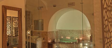 A modern bathroom with a glass-enclosed shower, a bathtub with lights, and a mosaic-tiled wall.