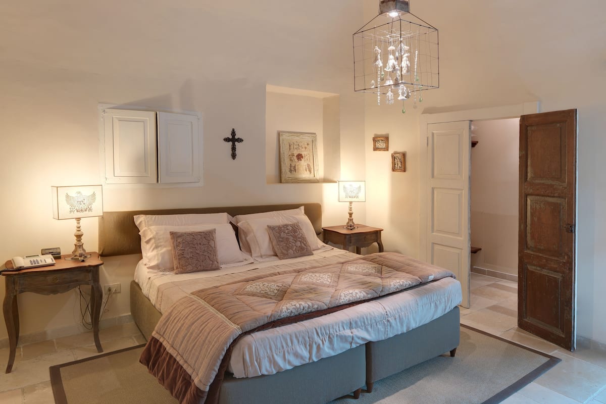 A bedroom with a bed, bedside tables, a cross on the wall, and a chandelier.