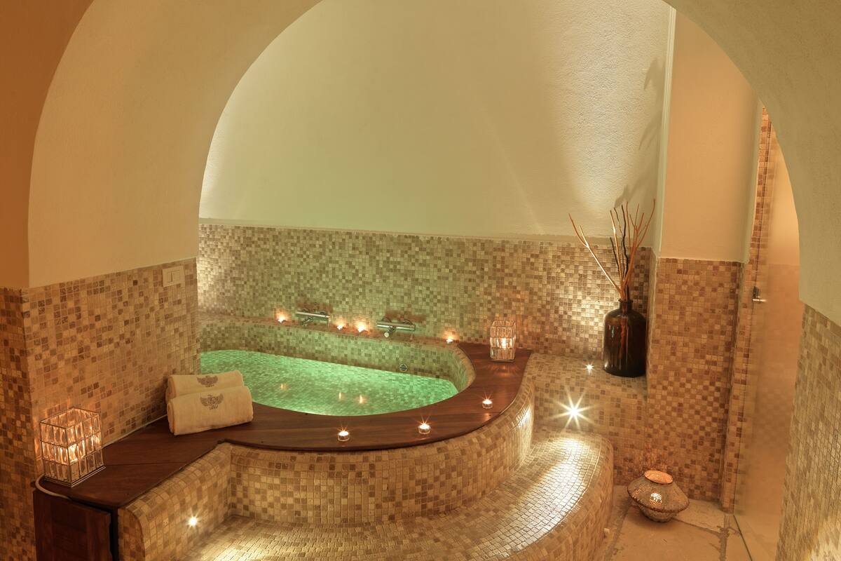 A spa area with a mosaic-tiled wall, a wooden bench, candles, and a glass container.