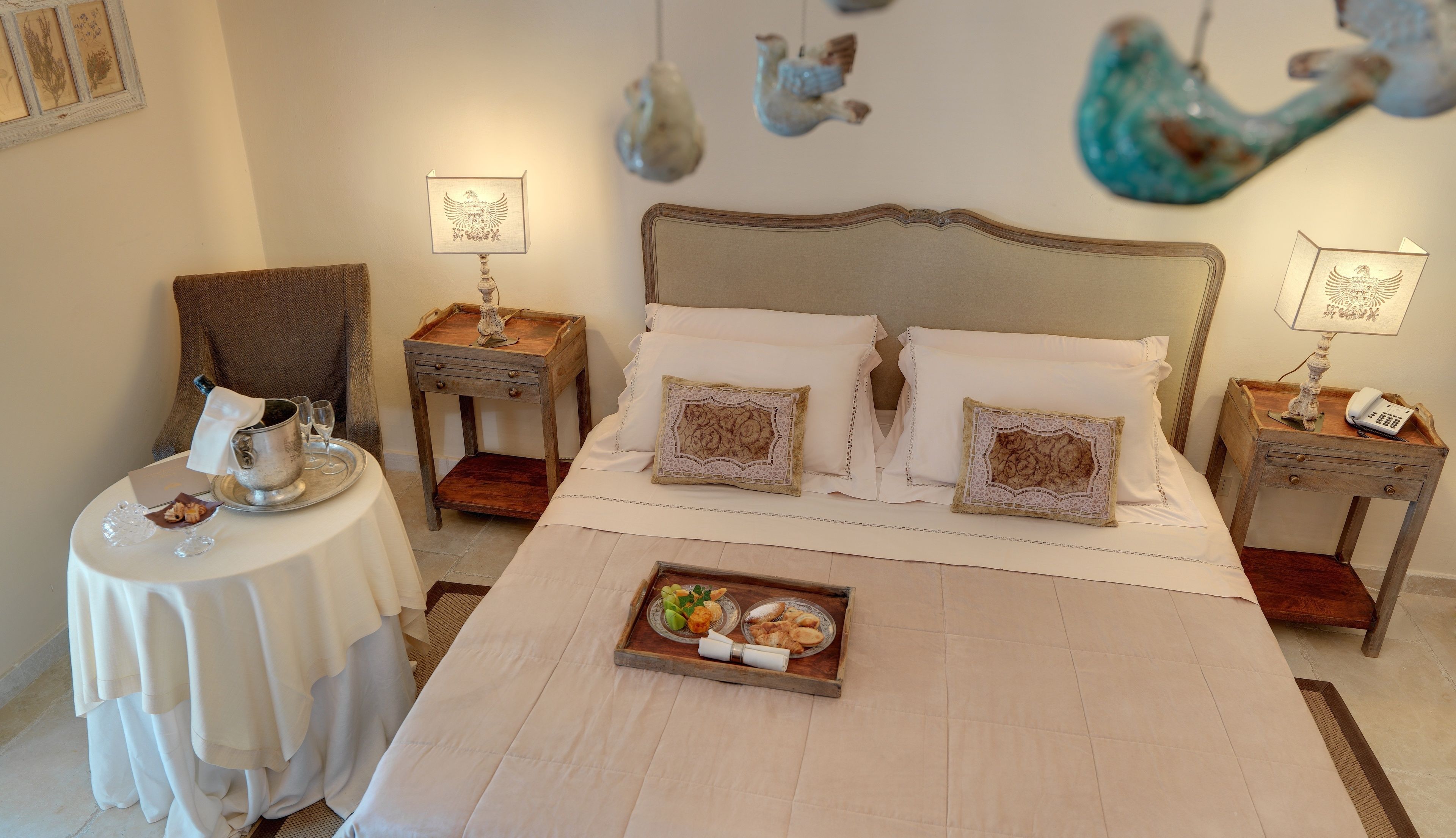 A hotel room with a large bed, two nightstands, a small table with a tray of food, and decorative wall art.