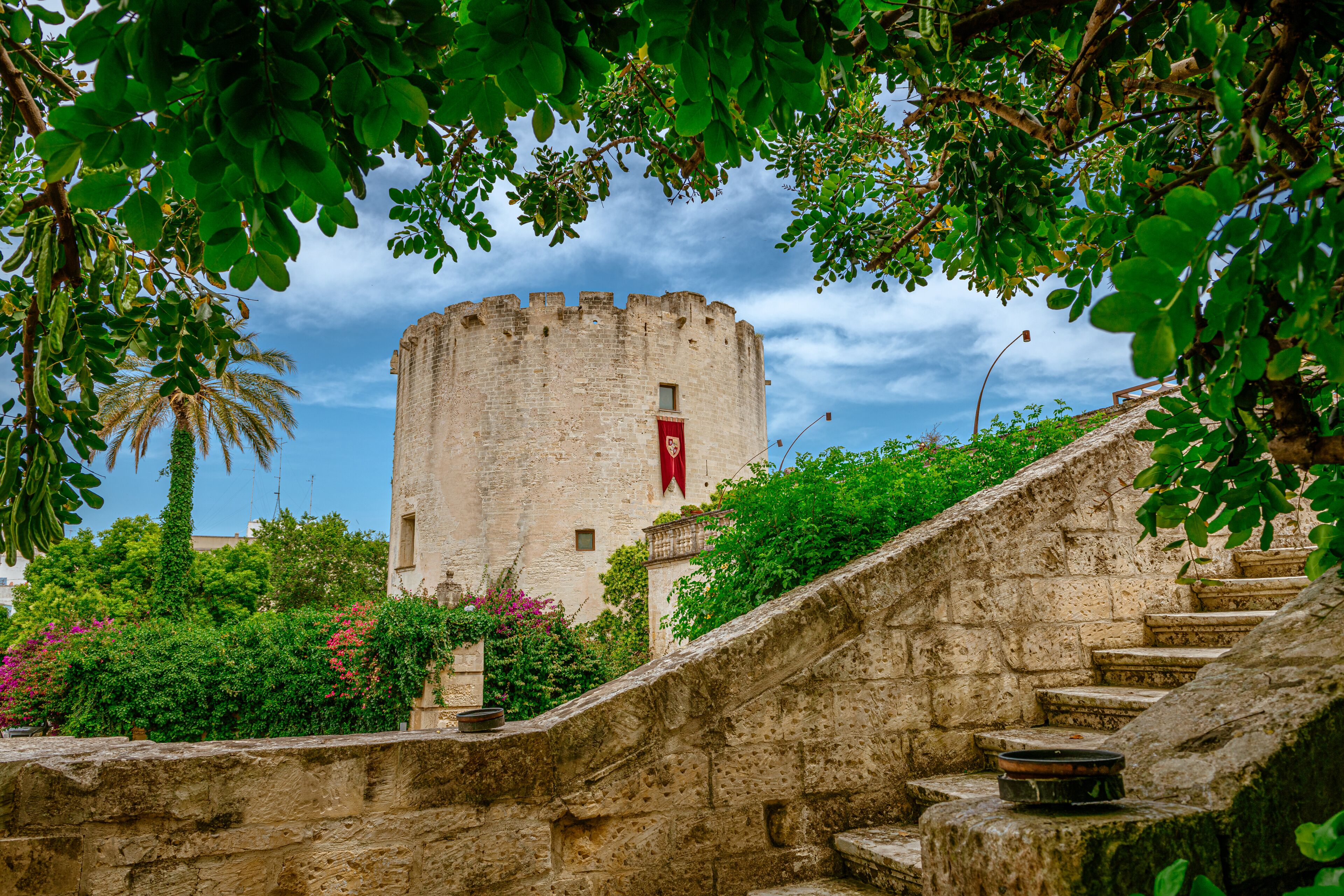 Una escalera de piedra conduce a una torre histórica con una bandera roja, rodeada de abundante vegetación.