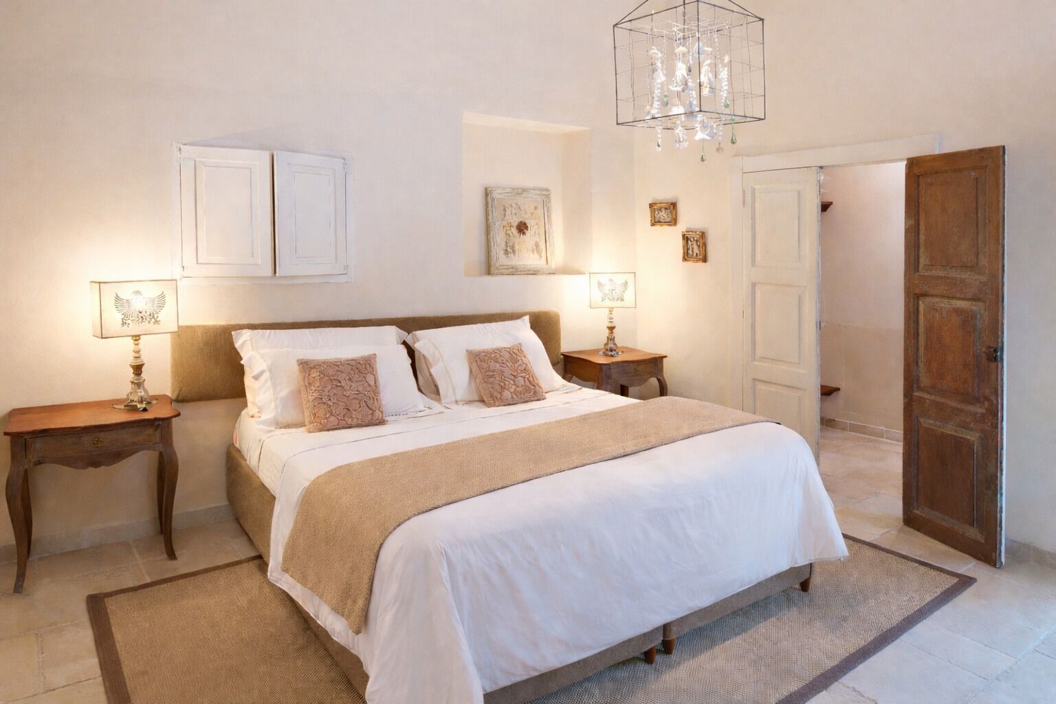 A bedroom with a large bed, two bedside tables, a chandelier, and a door.