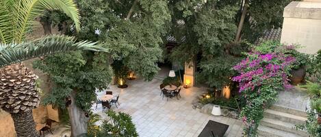 An outdoor patio area with tables and chairs, surrounded by lush greenery and trees.