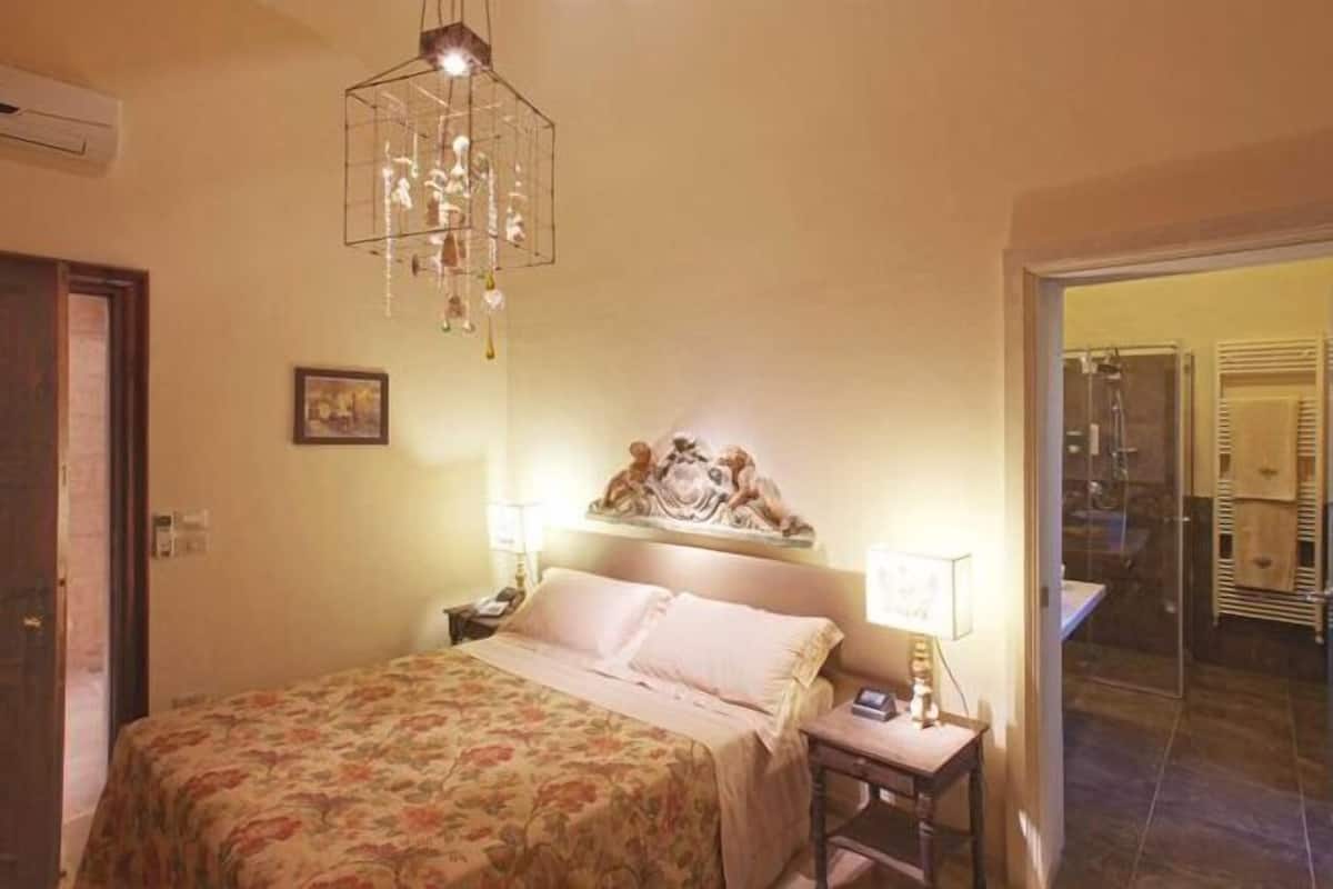 A bedroom with a bed, bedside lamps, a decorative wall piece, and an air conditioning unit.