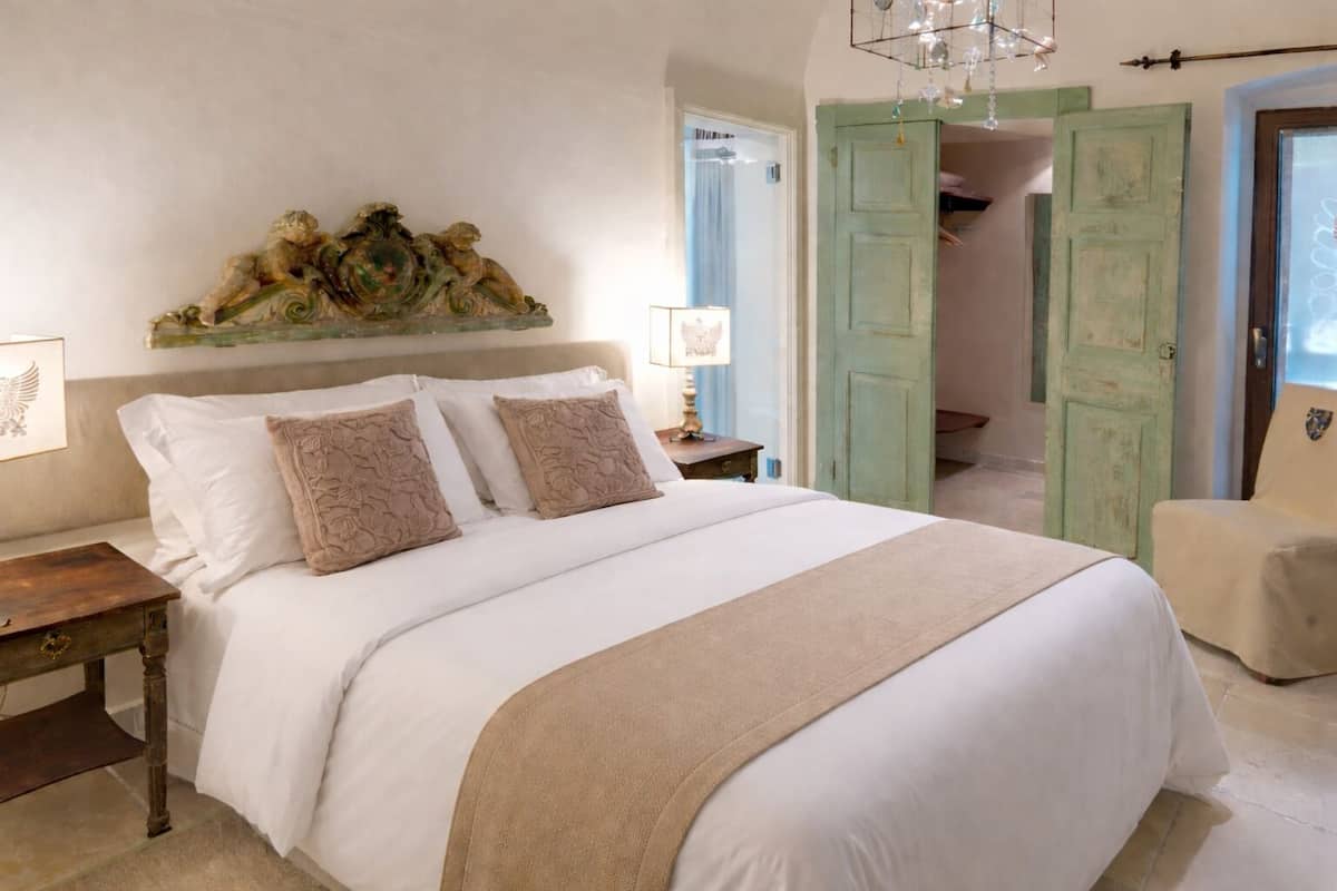 A bedroom with a large bed, a nightstand, a lamp, and a decorative piece above the bed.
