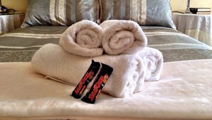 A neatly made bed with two rolled towels and a barone chocolate bar. - Pilgrims Delight (Centurion)
