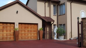 A two-story house with a garage, a large potted plant, and a statue in front. - Pilgrims Delight (Centurion)