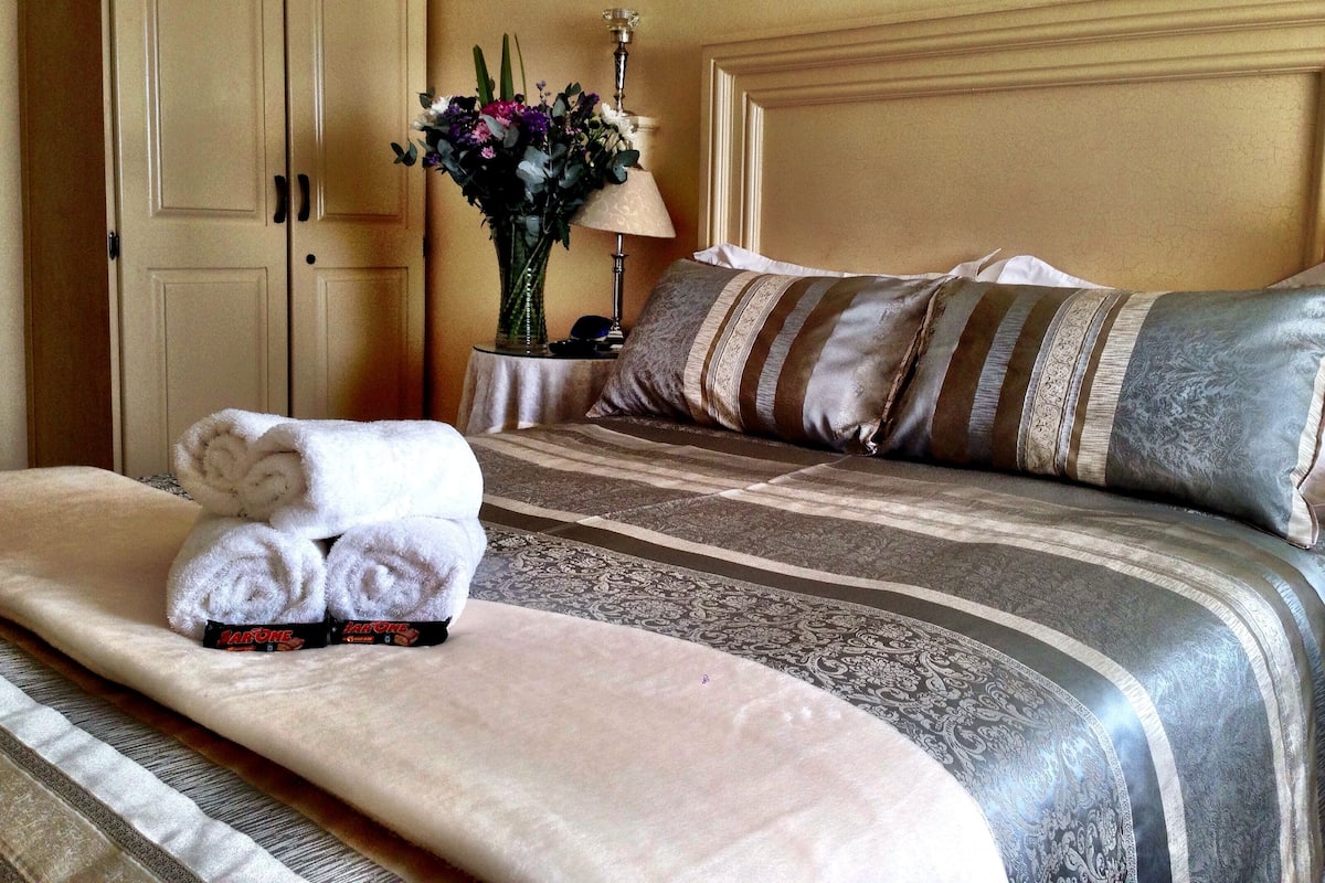 A neatly made bed with striped bedding, a vase with flowers, and a lamp on a bedside table.