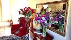 A room with a red armchair, two vases with flowers, a large mirror, and a patterned rug. - Pilgrims Delight (Centurion)