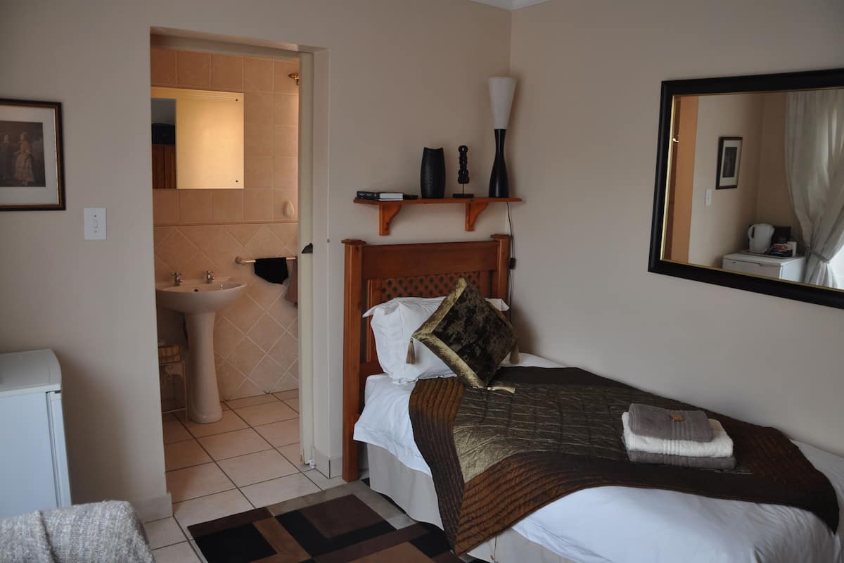 A bedroom with a bed, a bedside table, a mirror, a shelf with decorative items, and a bathroom with a sink and toilet.