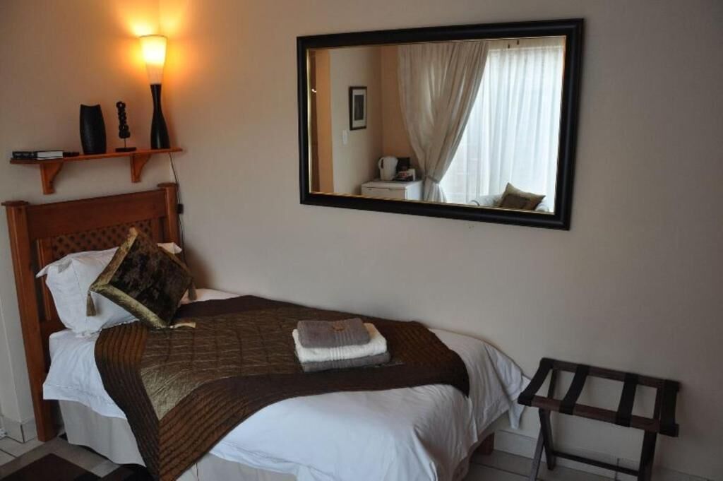 Un lit bien fait, avec une tête de lit, une lampe de chevet, un miroir et une petite table avec une chaise.
