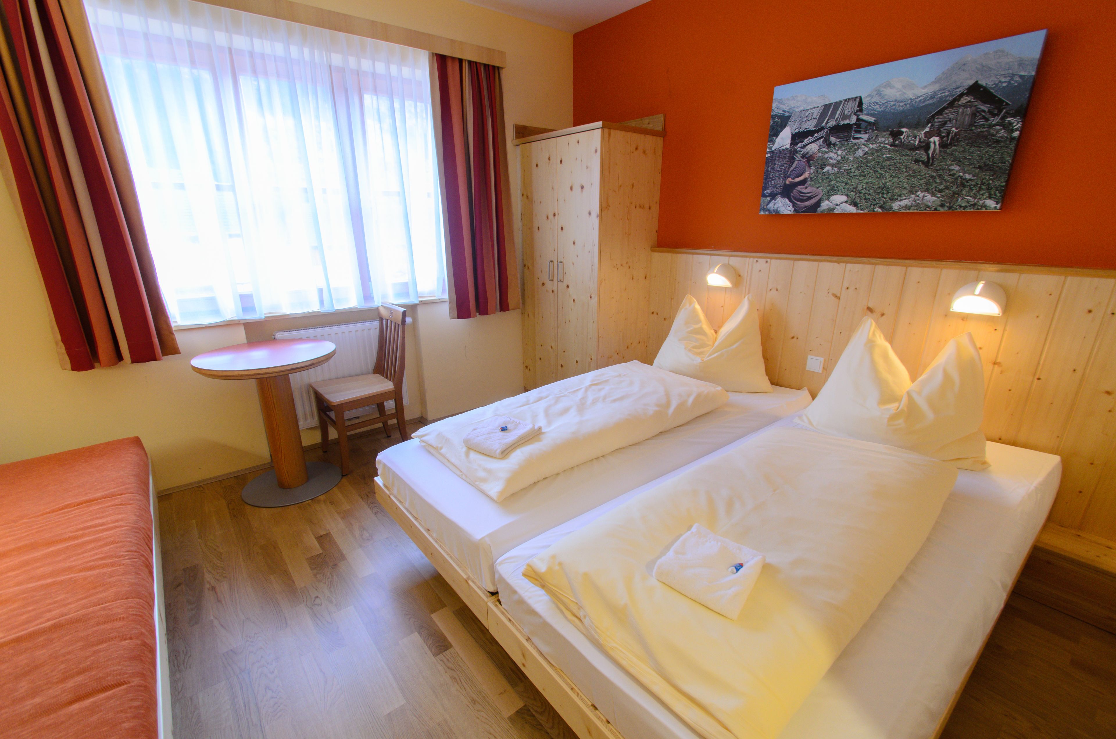 Habitació d'hotel amb dos llits, un armari de fusta, una taula rodona petita i una cadira.