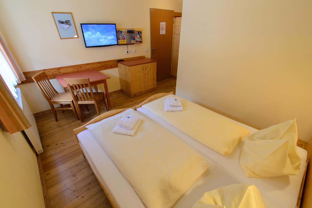 A room with two beds, a wooden table, a chair, a television, and a bulletin board.