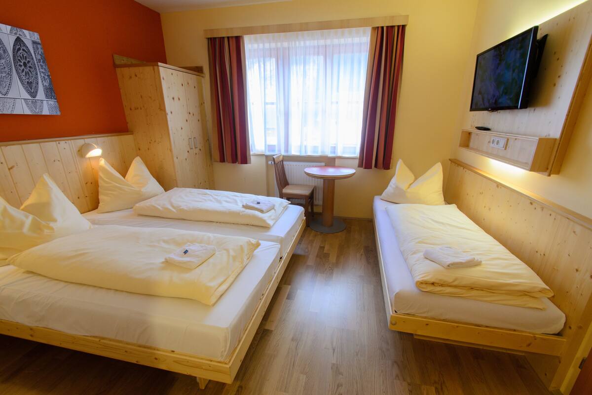 A hotel room with two beds, a small table, and a TV mounted on the wall.