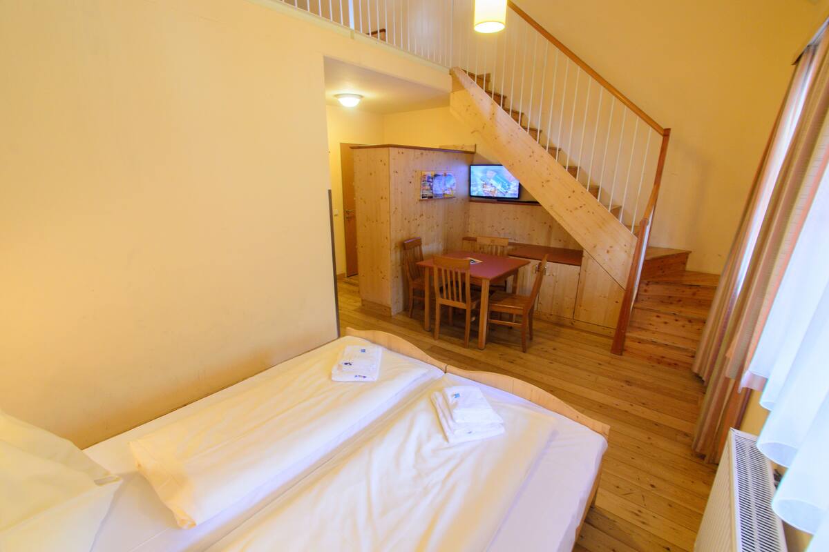 A room with a bed, a wooden table with chairs, and a staircase.