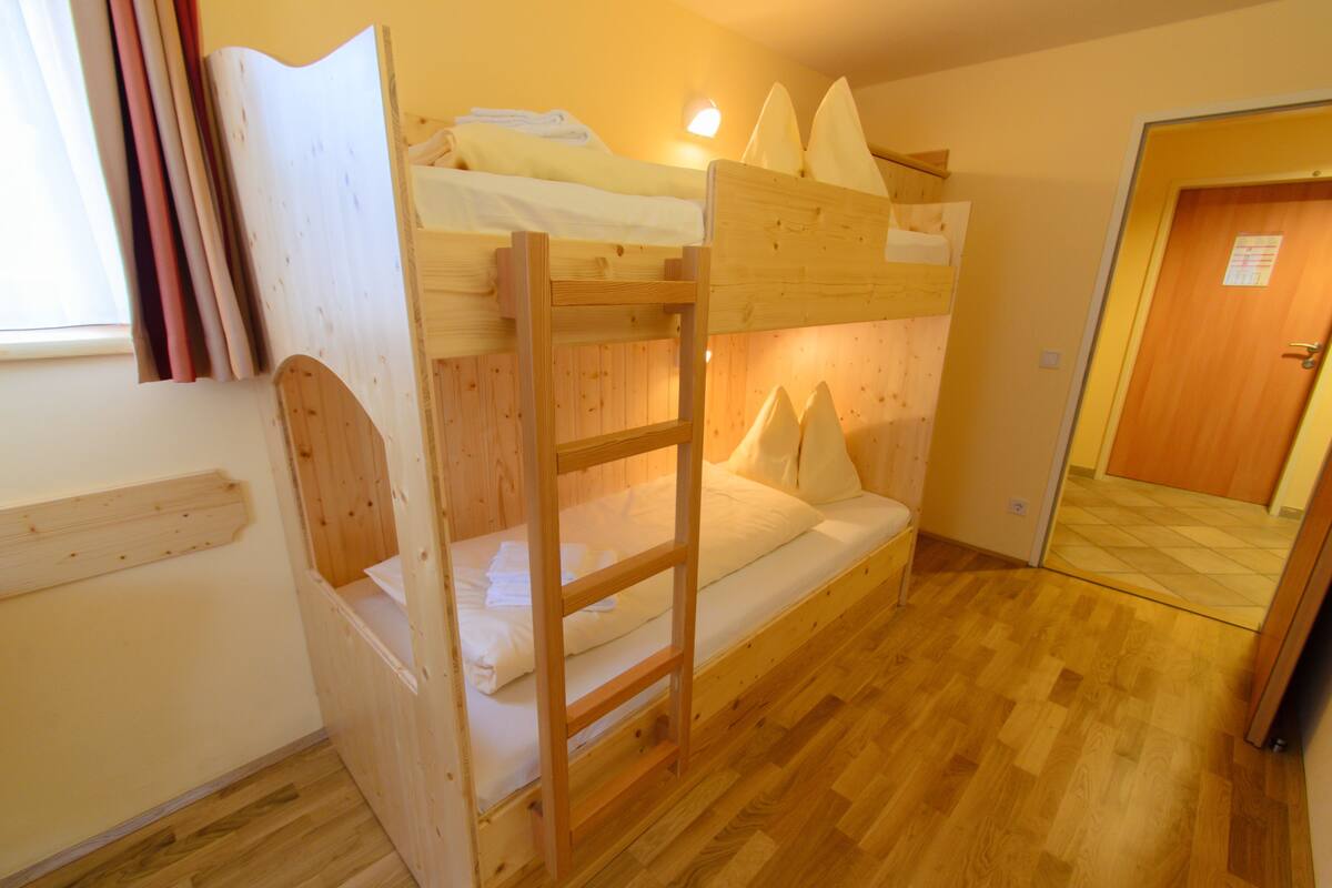 A bunk bed room with a wooden ladder, a small bedside table, and a window with curtains.
