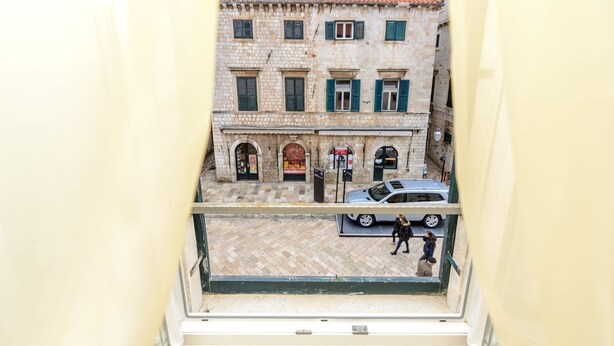 A view from a balcony overlooking a street with a building featuring arched windows and a tiled roof. - Studio Apartments Stradun (Dubrovnik)