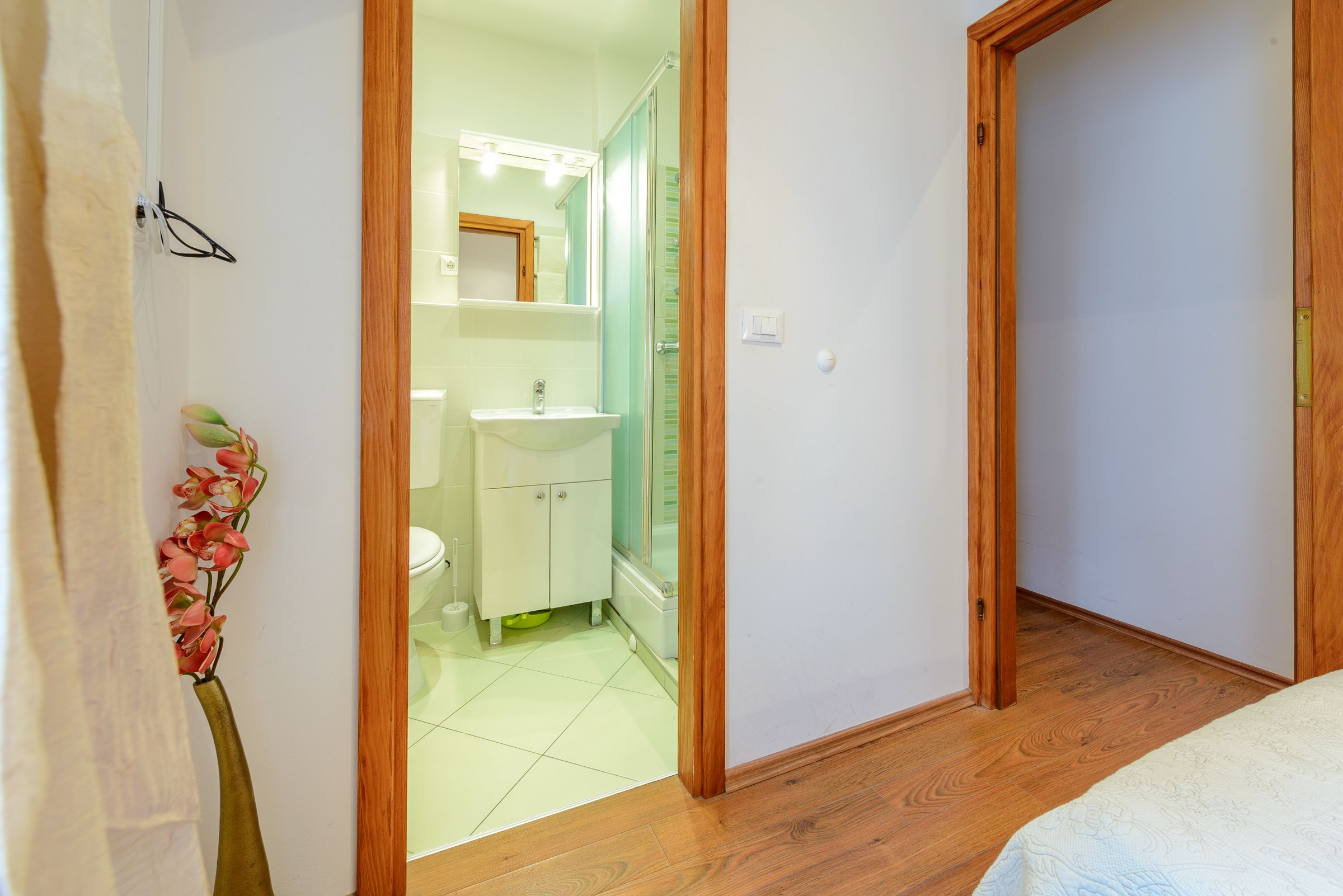 A narrow hallway leading to a bathroom with a sink, mirror, and shower.