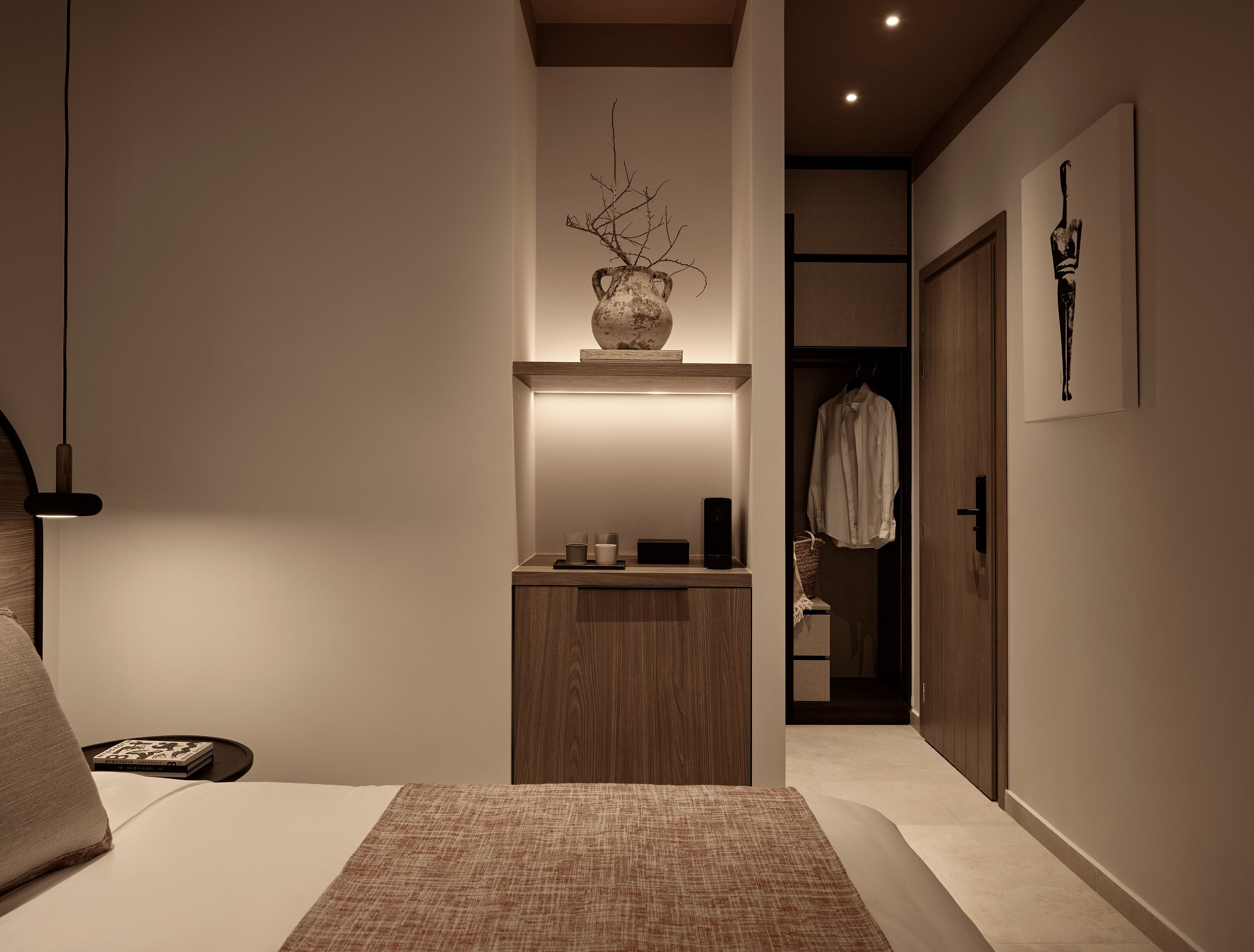 A bedroom with a bed, bedside table, lamp, and a small wooden cabinet with a vase.