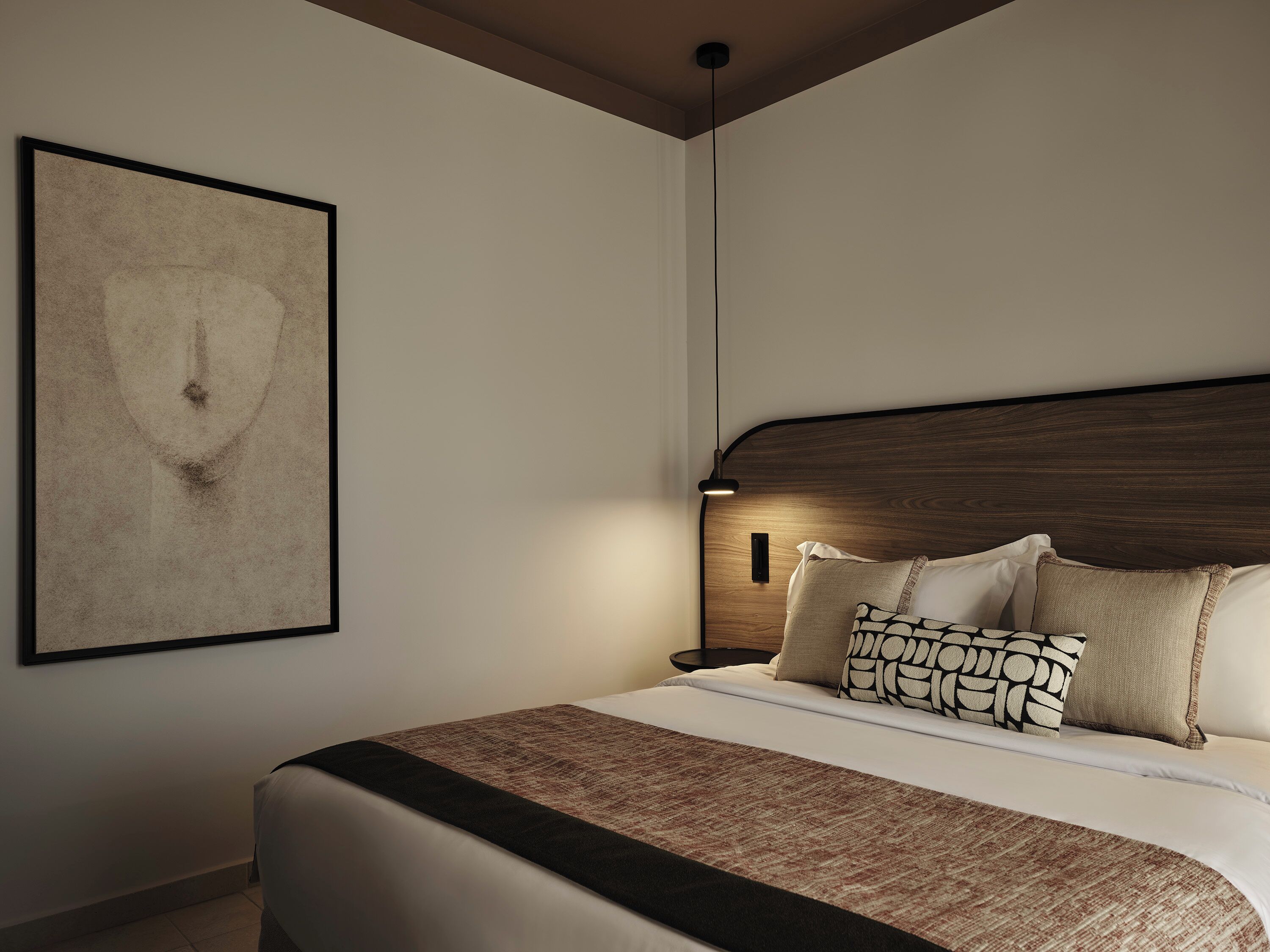 Ein modernes Schlafzimmer mit einem großen Bett, einem Kopfteil, einem Nachttisch und einem an der Wand befestigten Kunstwerk.