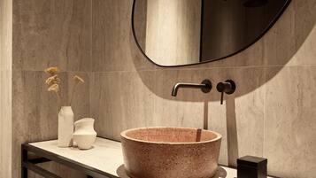 Un baño moderno con un lavabo de piedra redonda, un espejo y un perchero para toallas.