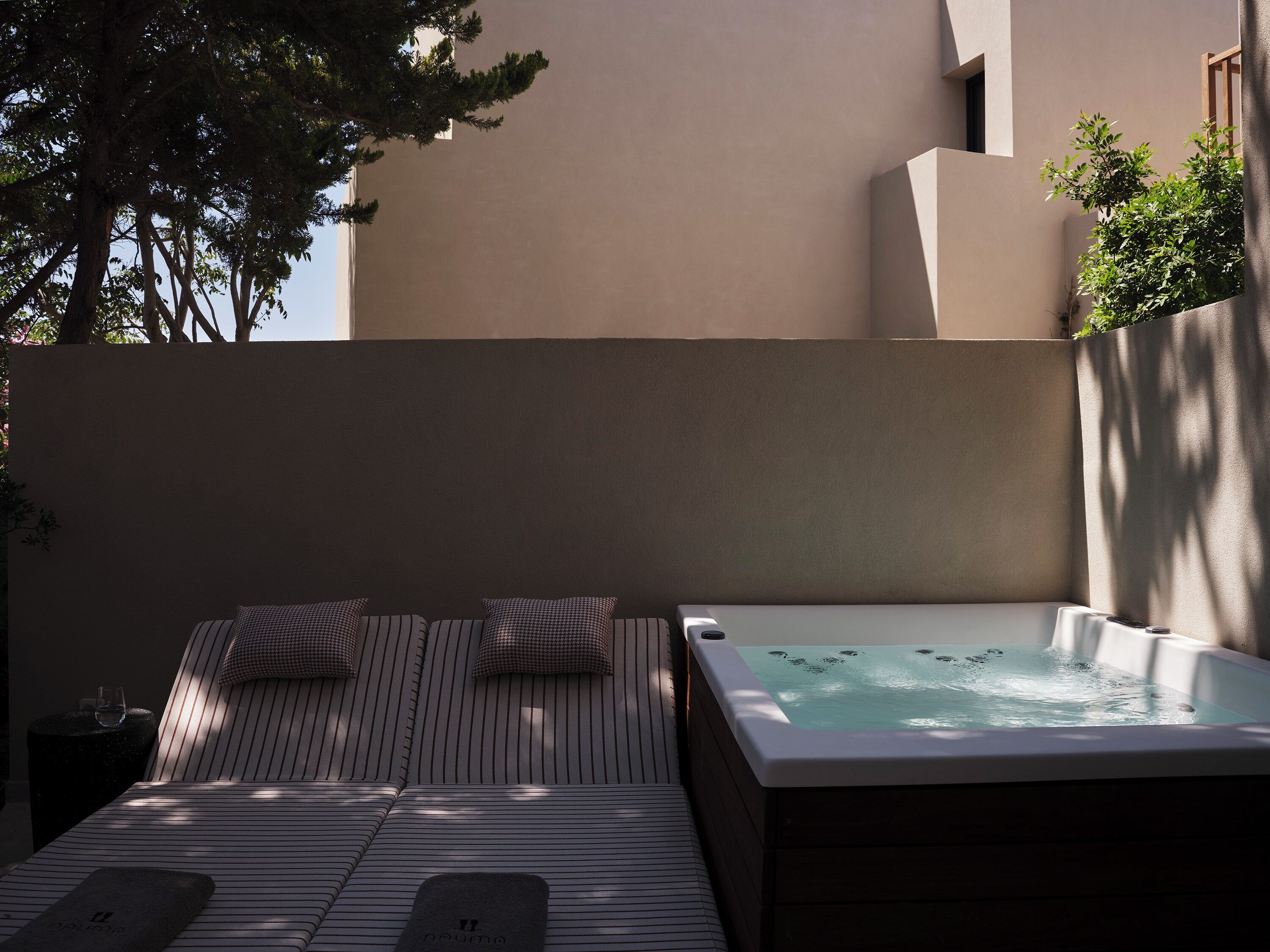 A spa area with a hot tub, a lounge with striped cushions, and a view of a building with a beige facade.